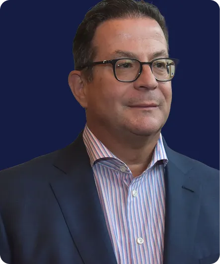 Middle-aged man wearing glasses, navy blazer, and striped shirt against dark blue background.