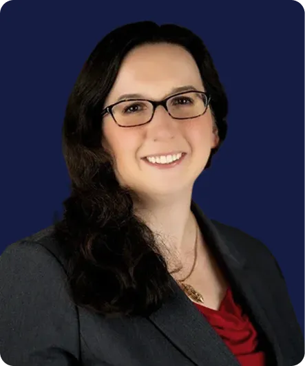 Professional headshot of a smiling woman with glasses, dark hair, and business attire.