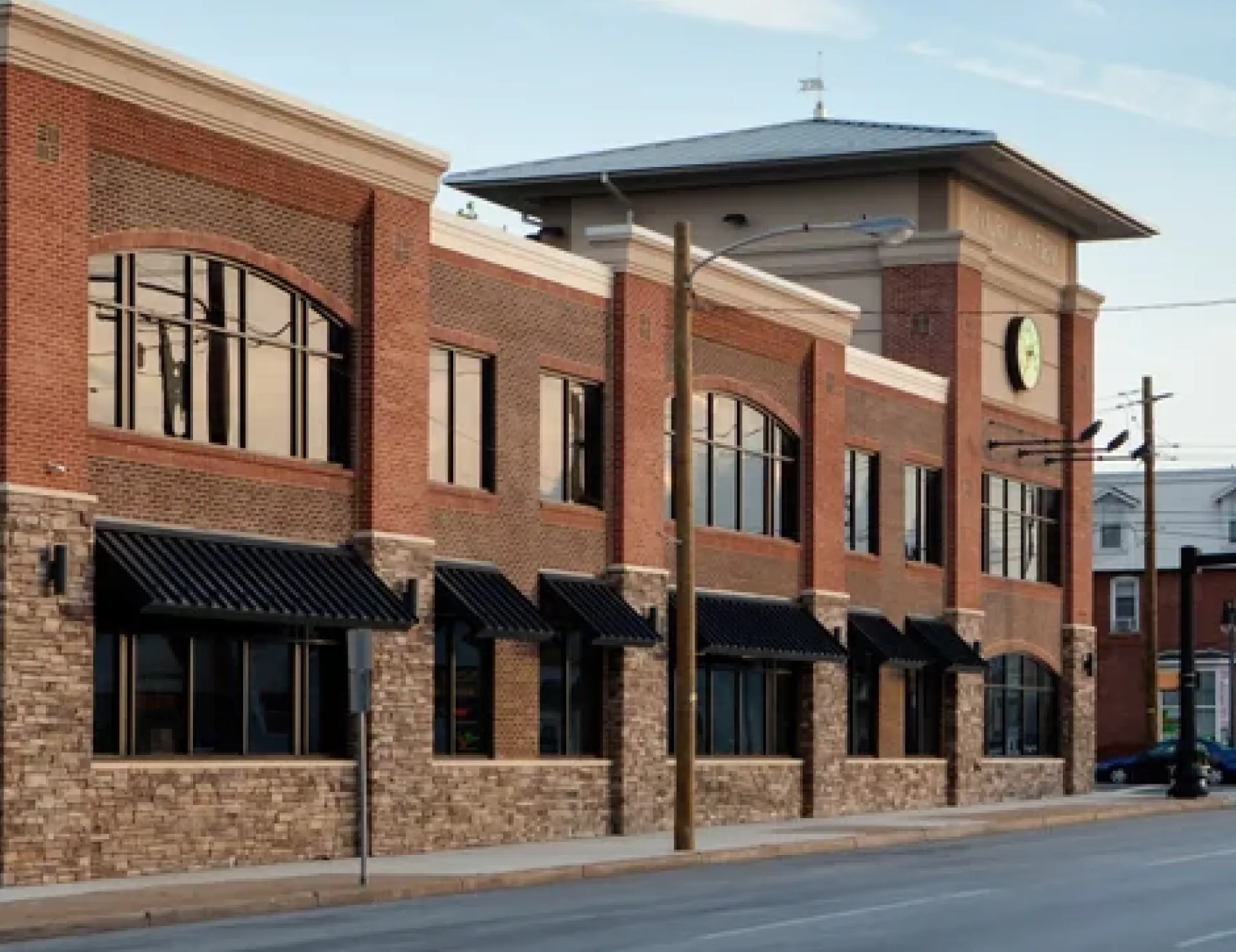 Two-story brick commercial building with large windows and black awnings, clock tower visible.