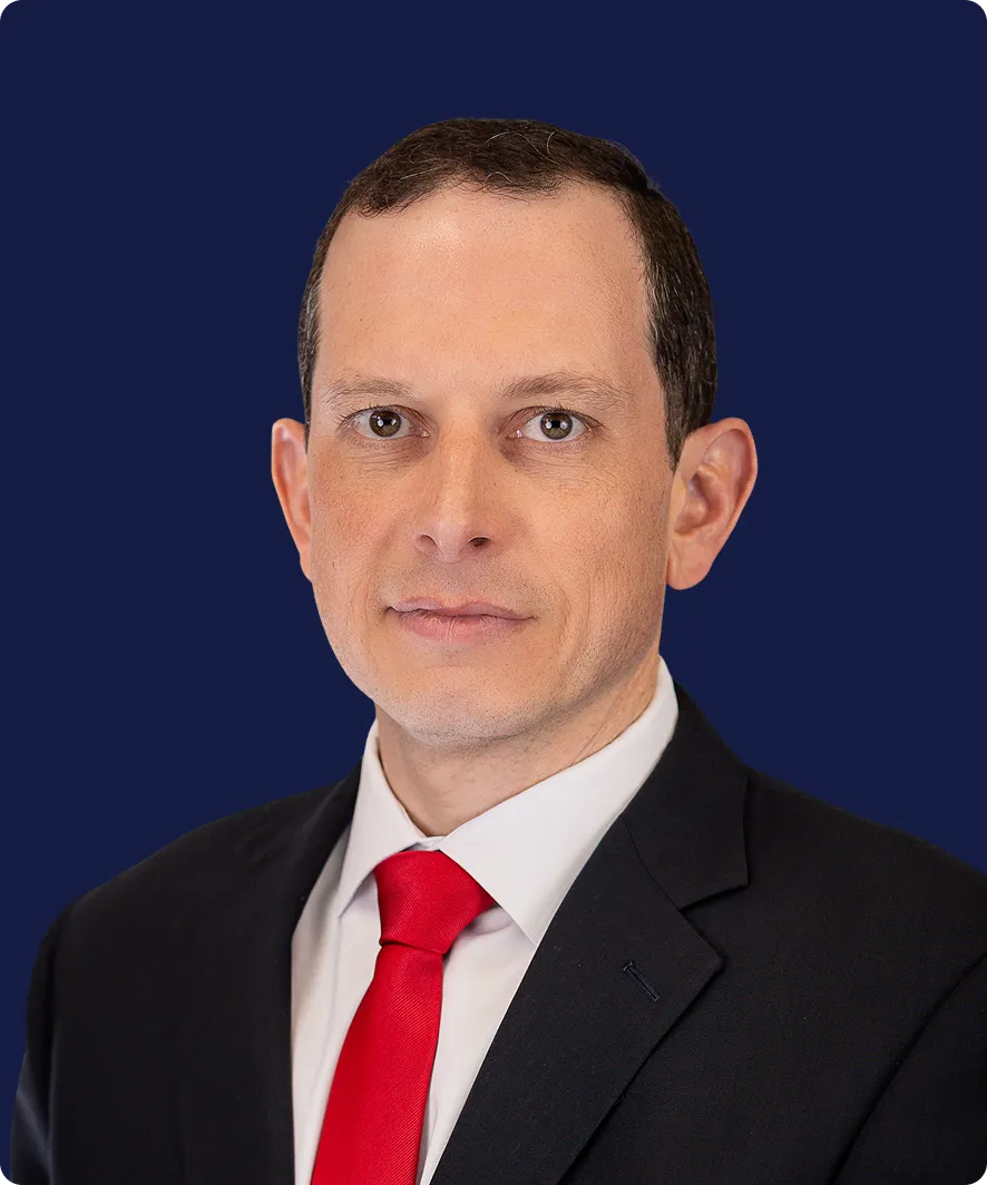 Professional headshot of a man in a black suit, white shirt, and red tie against a dark blue background.