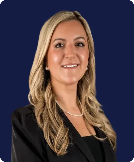Professional portrait of a smiling woman with long blonde hair wearing a black blazer and pearl necklace against a dark blue background.