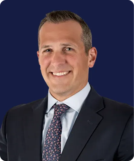 Professional headshot of a smiling man in a dark suit and patterned tie against a solid navy background.