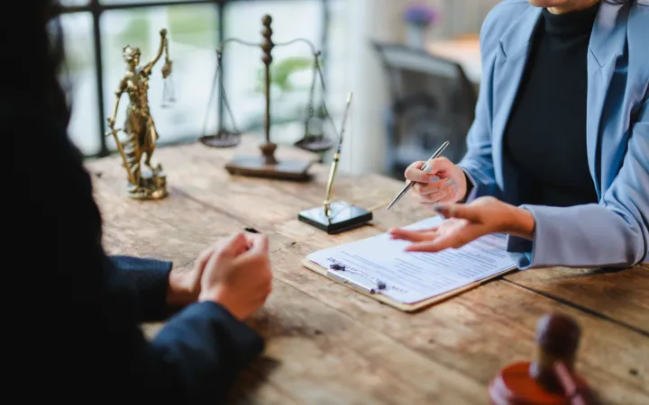 Two professionals discussing a document at a wooden desk with legal scales and a gavel.