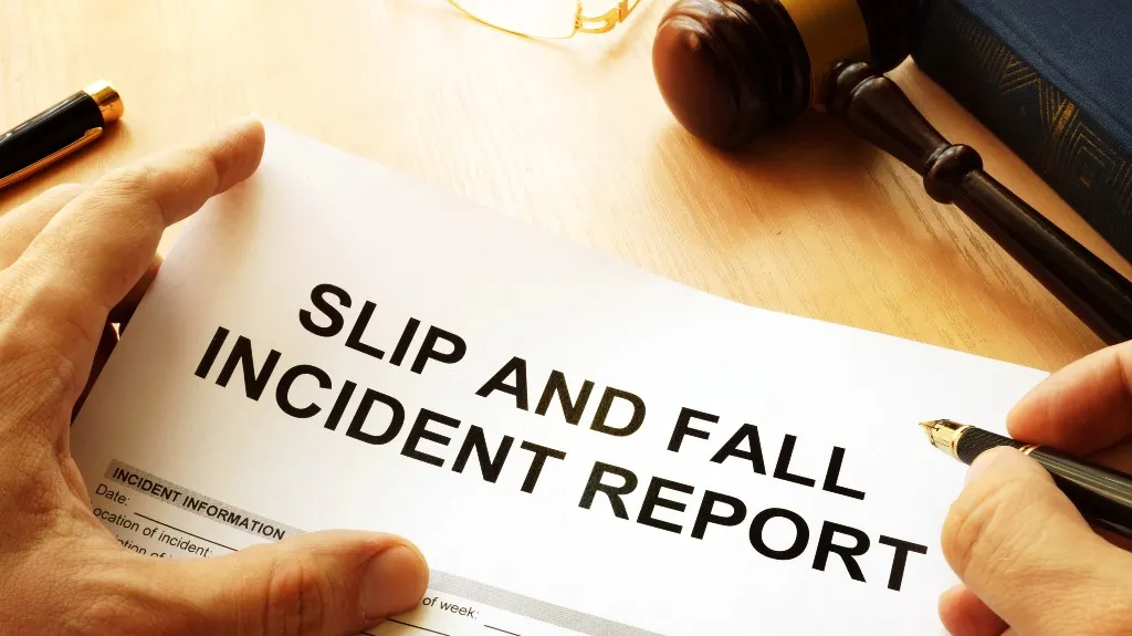 Close-up of hands holding a slip and fall incident report form with a pen and a judge's gavel nearby.
