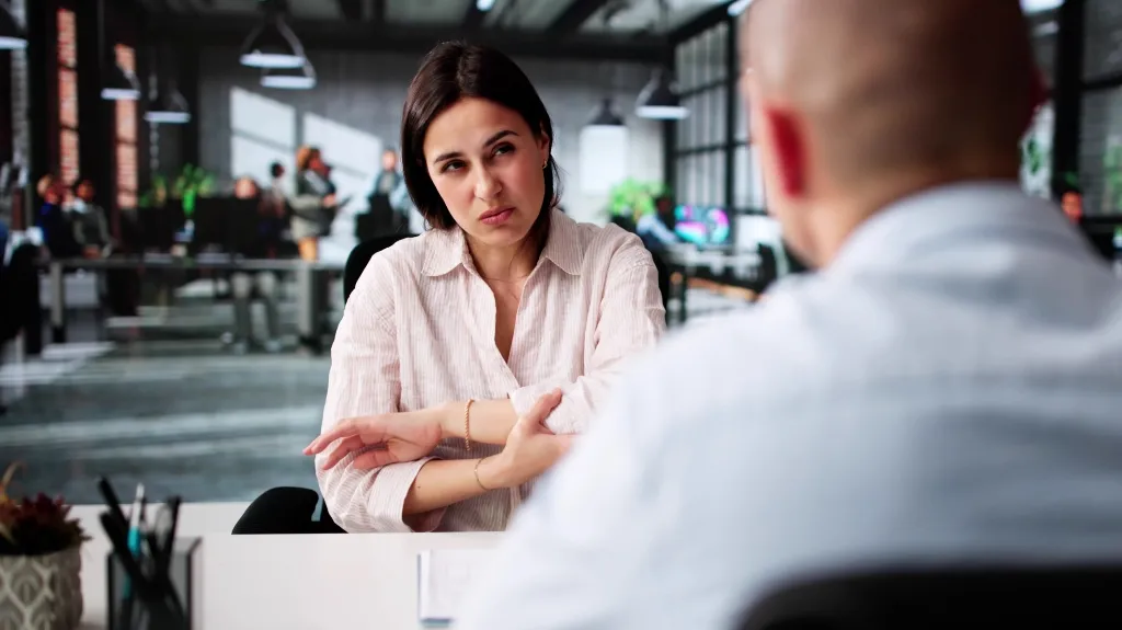 Professional woman in white blouse expressing concern during office conversation with male colleague.