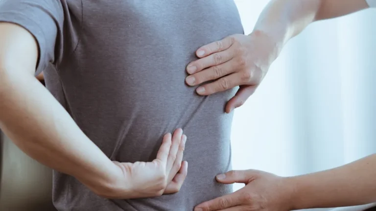 Close-up of hands examining a person's lower back through a gray shirt.