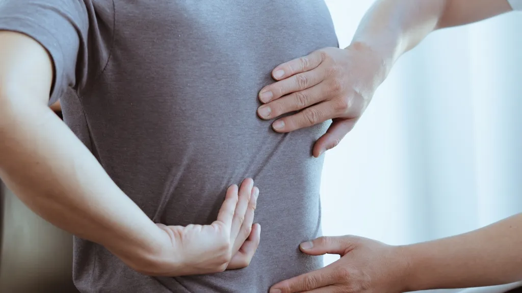 Close-up of hands examining a person's lower back through a gray shirt.