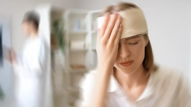 Woman with head bandage holding forehead in medical office, blurred healthcare professional in background.